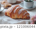 Golden brown croissant with flaky layers, dusted with powdered sugar, perfect for breakfast or snack. Enjoy its buttery texture and delightful taste 121006044