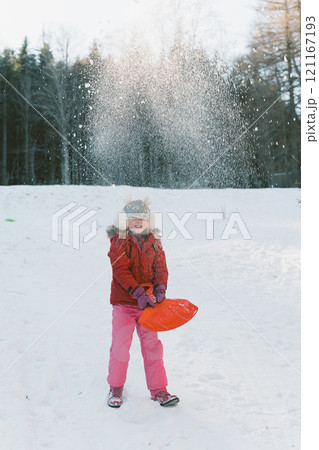 Little girl in a red jacket and earmuffs throws snow into the air 121167193