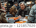 A writer author of books signs autographs in a bookstore among stacks of literary works. 121857020