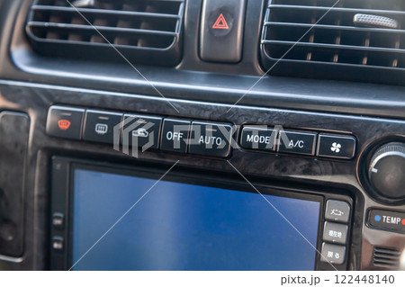 Close-up of the center console on a gray panel inside the car, with climate control and a red emergency button. Setting up and refueling the air conditioner in the workshop. 122448140