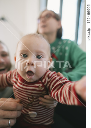 A Joyful Baby is Reaching Out with Family Happily in the Background, Spreading Cheer 122466906