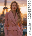 A woman wearing a pink coat stands in front of the Eiffel Tower 122437060