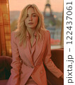 A blonde woman is sitting on a couch in a pink jacket 122437061