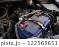 Close-up view of a car battery with connected jumper cables, highlighting vehicle maintenance and repair in progress. 122568651