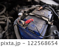 Close-up of a car battery with a red jumper cable attached, highlighting electrical repair and vehicle maintenance in progress. 122568654