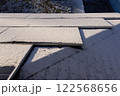 Snow-covered solar panels on a rooftop illuminated by sunlight, with a frosty backyard visible in the background. 122568656