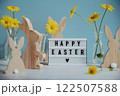 Phrase HAPPY EASTER traditional greeting to christian holiday. Festive mood composition with bunnies and yellow flowers on pastel blue background. Sustainable 122507588