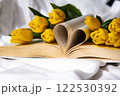 Book pages in shape of heart symbol love with bouquet of pink tulips on messy bed. Romantic morning scene. Greeting card Holiday flowers springtime 122530392