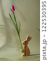 Pink fresh tulip in vase of Easter wooden bunny in green background with trendy deep shadows. Spring flowers in violet color. Postcard wallpaper design 122530395