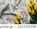 Bouquet of yellow tulips on messy bed. HELLO SPRING written text on wine glass. Romantic morning scene. Greeting card Holiday flowers springtime 122530398