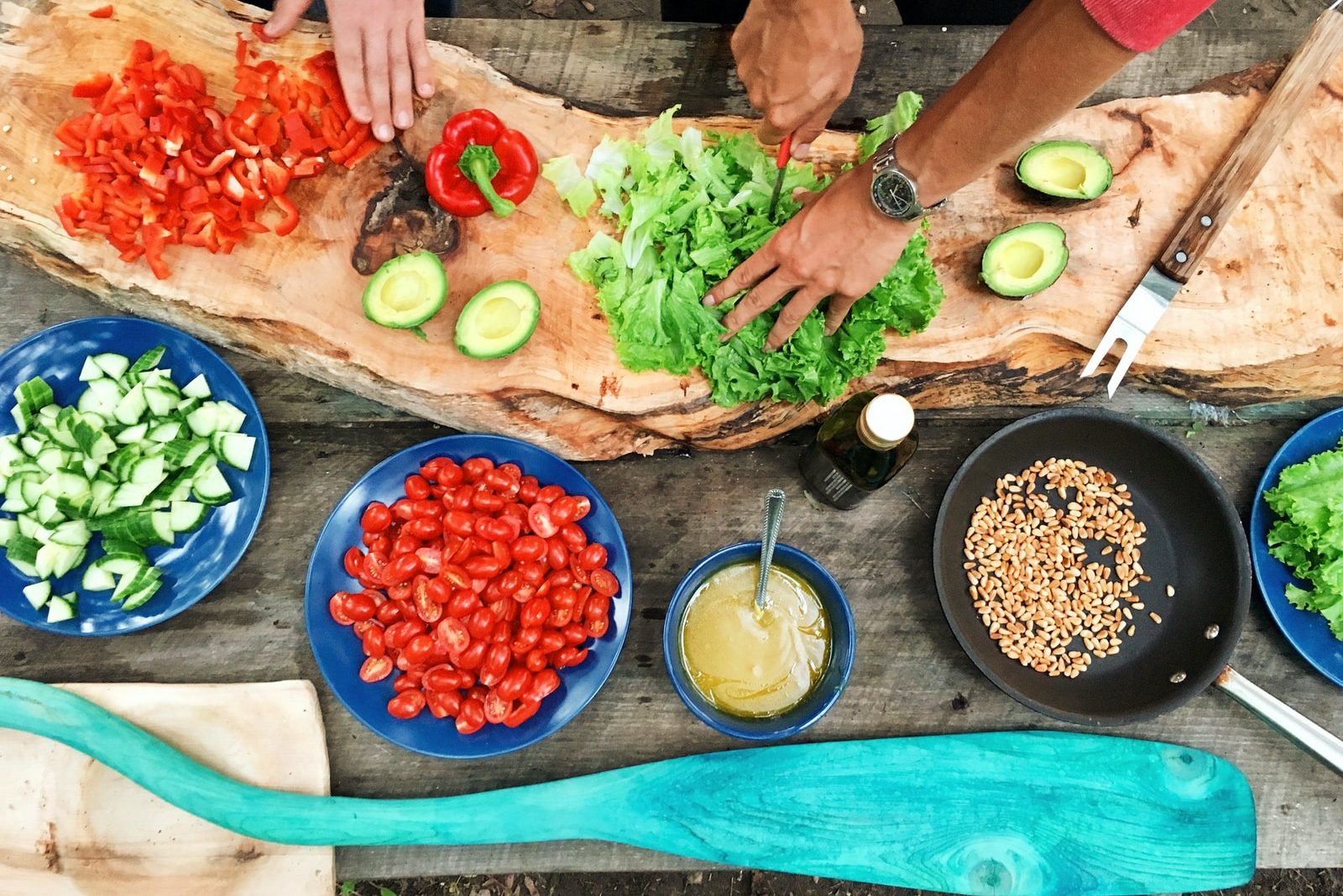 person slicing green vegetable in front of round ceramic plates with assorted sliced vegetables during daytime