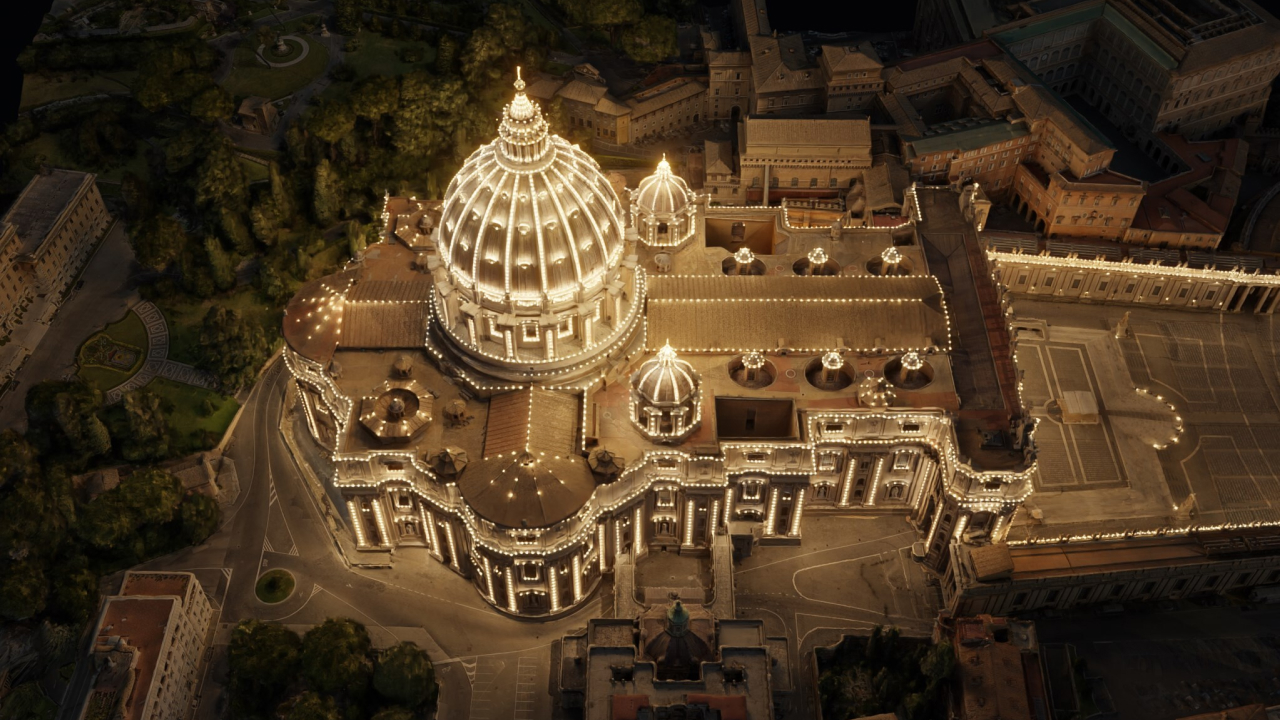 Aerial view of St. Peter's Basilica illuminated at night, showcasing its dome and surrounding structures.