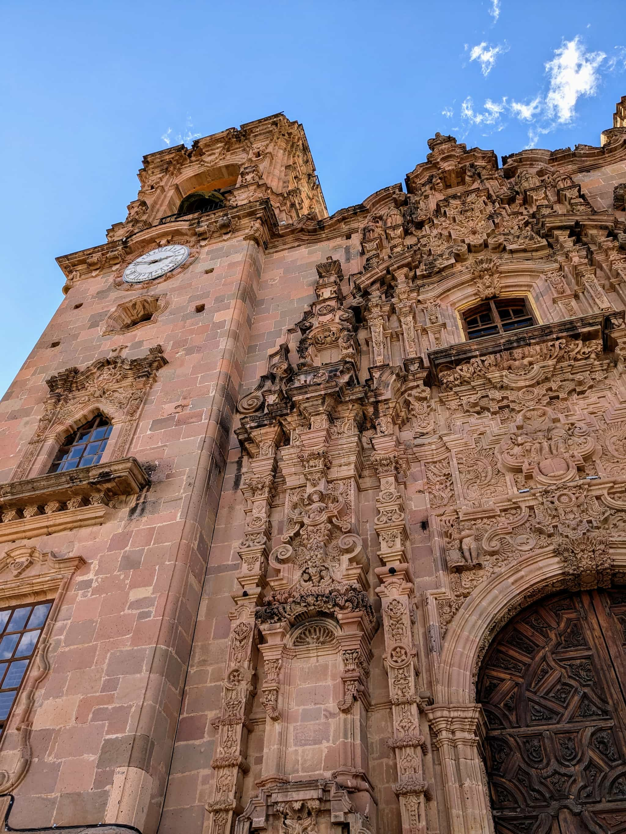 Looking up at an ornate church made of redish stone and a clear sky.