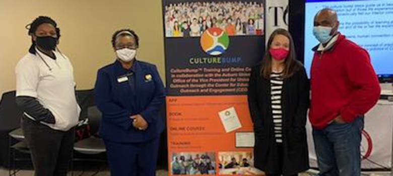 Four people wearing masks pose in front of sign