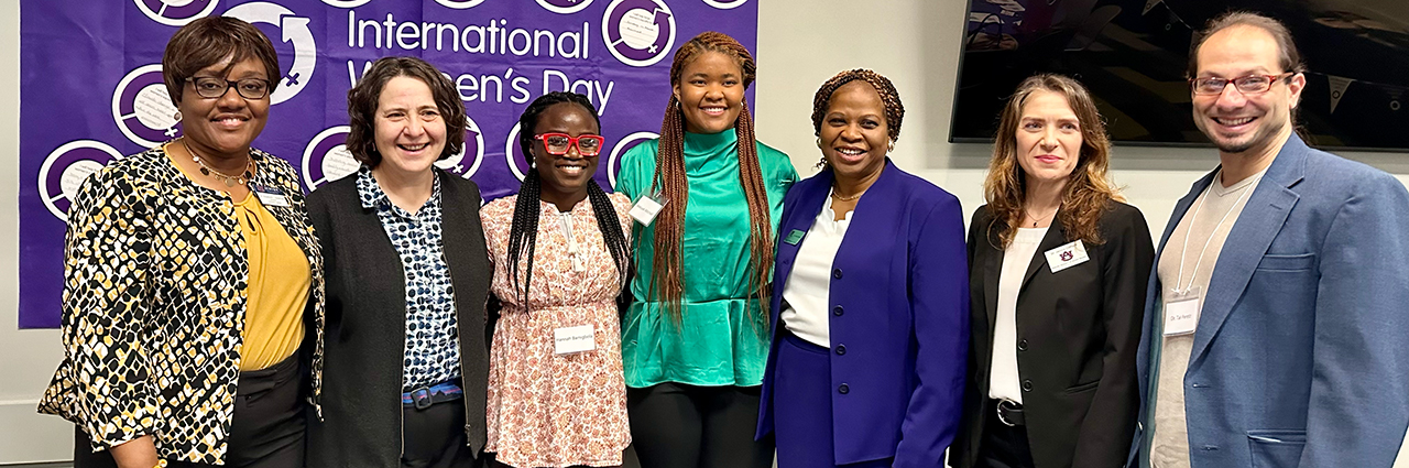 Six women and one man pose for a photo at an International Women's Day Conference.