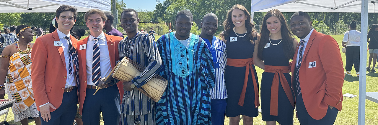 War Eagle Girls and the Auburn Plainsmen pose with Global Attire Showcase participants at Global Community Day Festival.