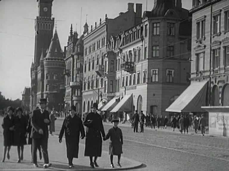 Stadsvy från 1920-talet, människor på trottoar och byggnader i bakgrunden.