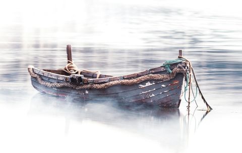 A weathered small boat in the fog, with ropes going into the water, hopefully leading to an anchor.
