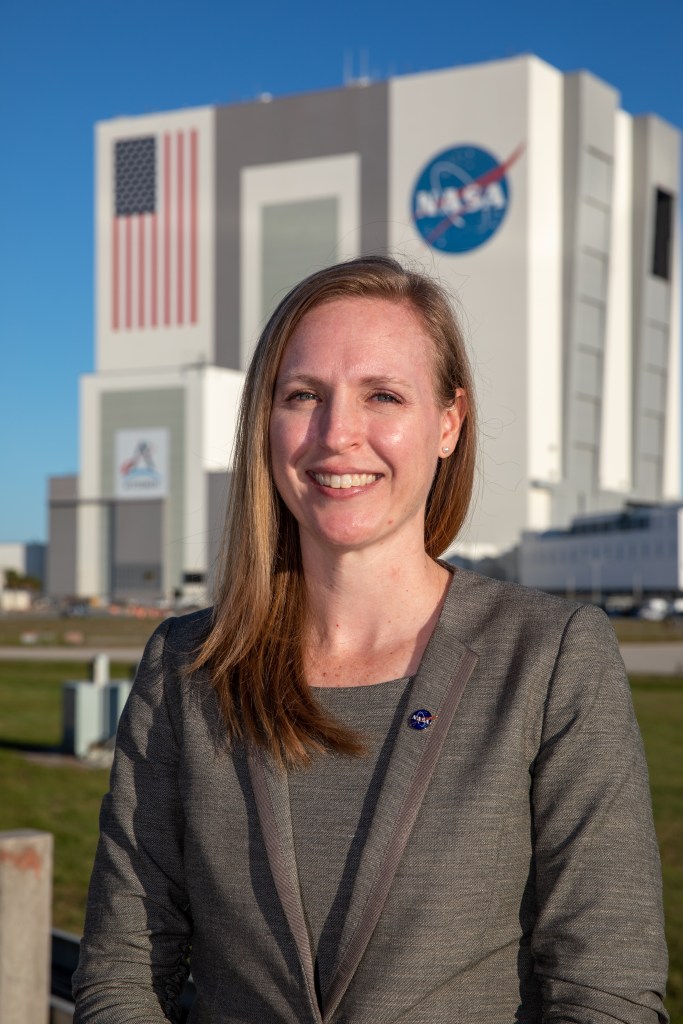 Kennedy Space Center's Allison Mjoen is photographed with the Vehicle Assembly Building in the background.