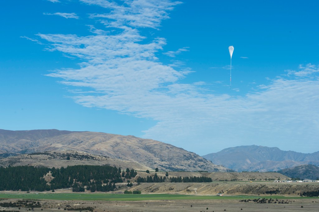 A landscape photo of New Zealand, with a partially inflated balloon in the shape of an upside down teardrop in the distance.