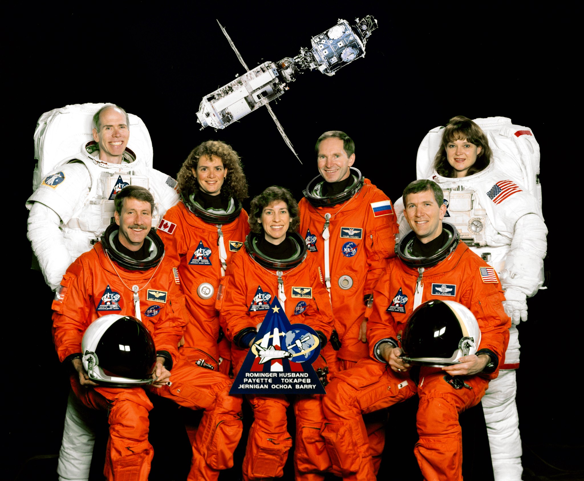 The crew of STS-96 in orange and white space suits pose for a portrait