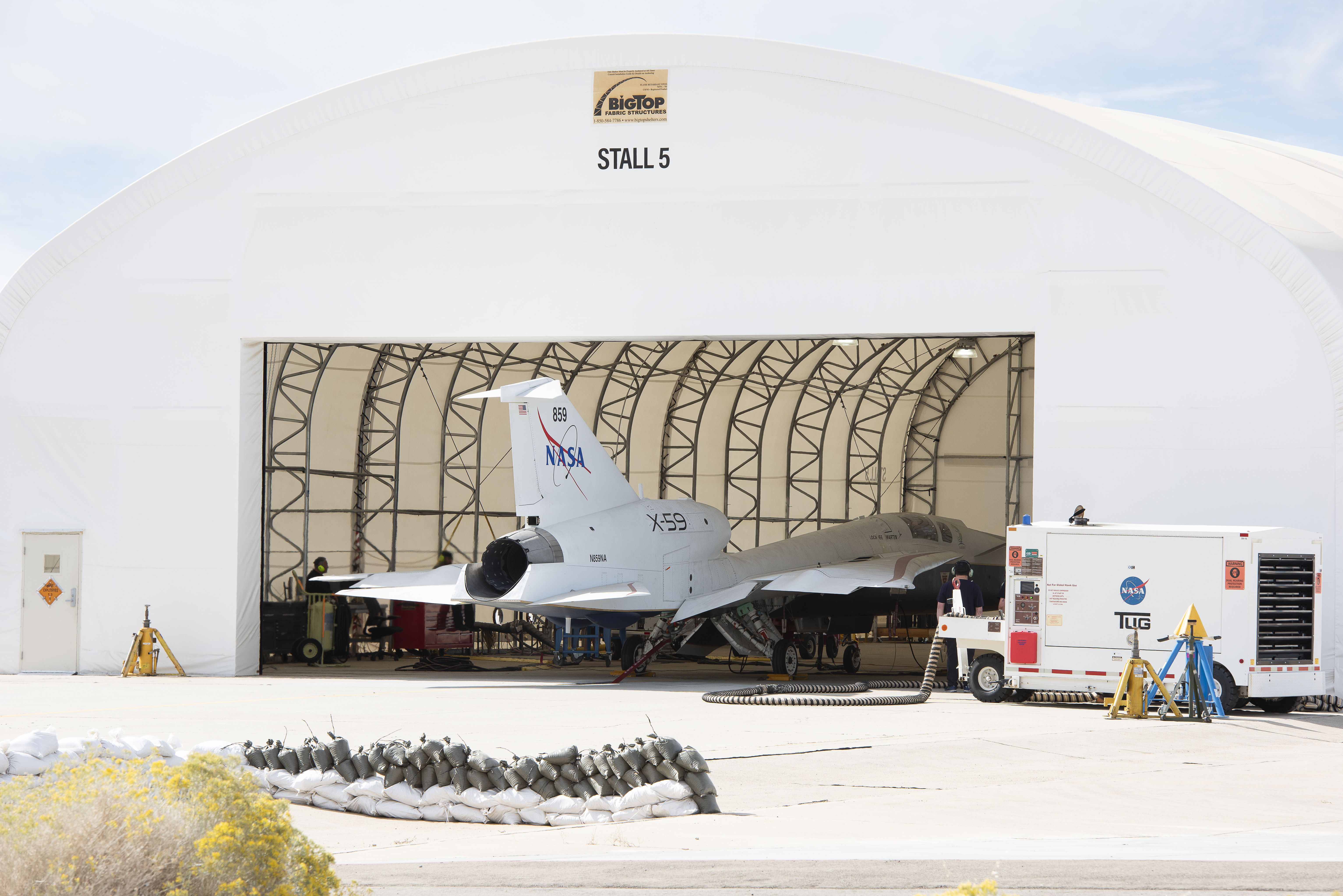 A white airplane sits inside of a white hangar with its nose facing inward.