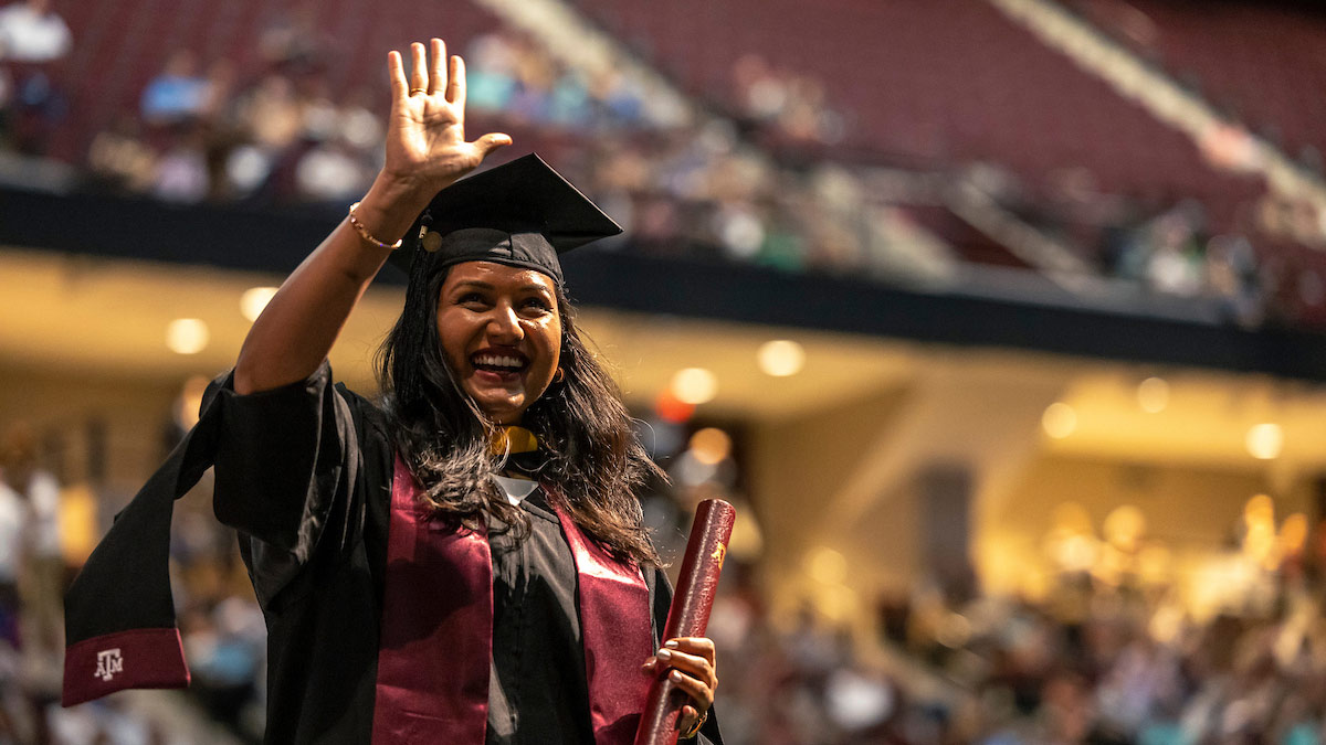 An Aggie graduate waves after she collects her diploma at graduation