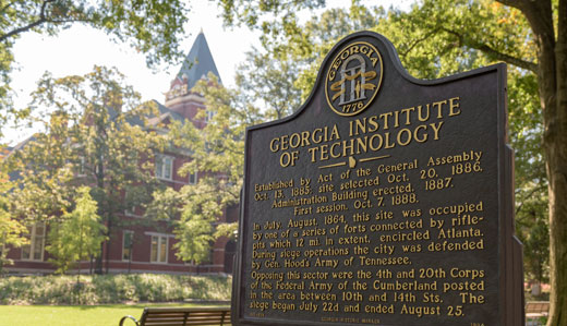 A sign detailing the history of the establishment of Georgia Tech is in the foreground, with campus greenery and Tech Tower in the background.