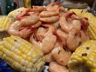 A plate piled high with boiled shrimp, surrounded by corns on the cob.