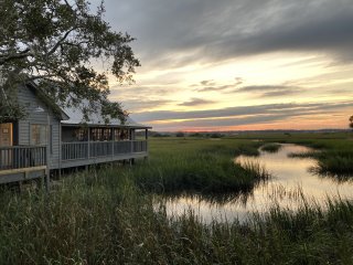 A wooden house at the edge of a swamp at sunset.