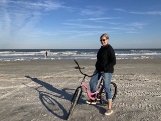 Jessica on a pink bike on a sandy beach, wrapped up warm.