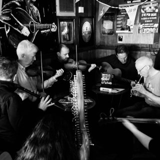 Two fiddlers surrounded by other musicians: whistle, flute, guitar, and even a harp.