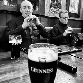 Two men playing tin whistles at a pub table with pints of Guinness and other musical instruments on it.