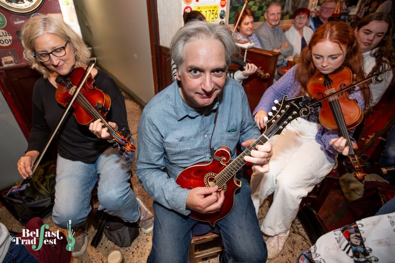 Me dressed in denim playing my red mandolin in a pub flanked by two women playing fiddle.