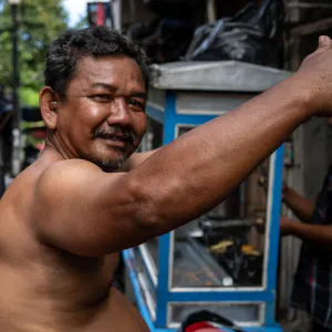 Shirtless man raising his arm up in front of a food stall