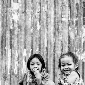 Two girls sitting in front of corrugated wall