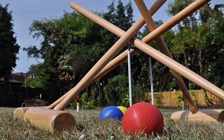 Colorful croquet balls and wooden mallets leaning against each other in the grass