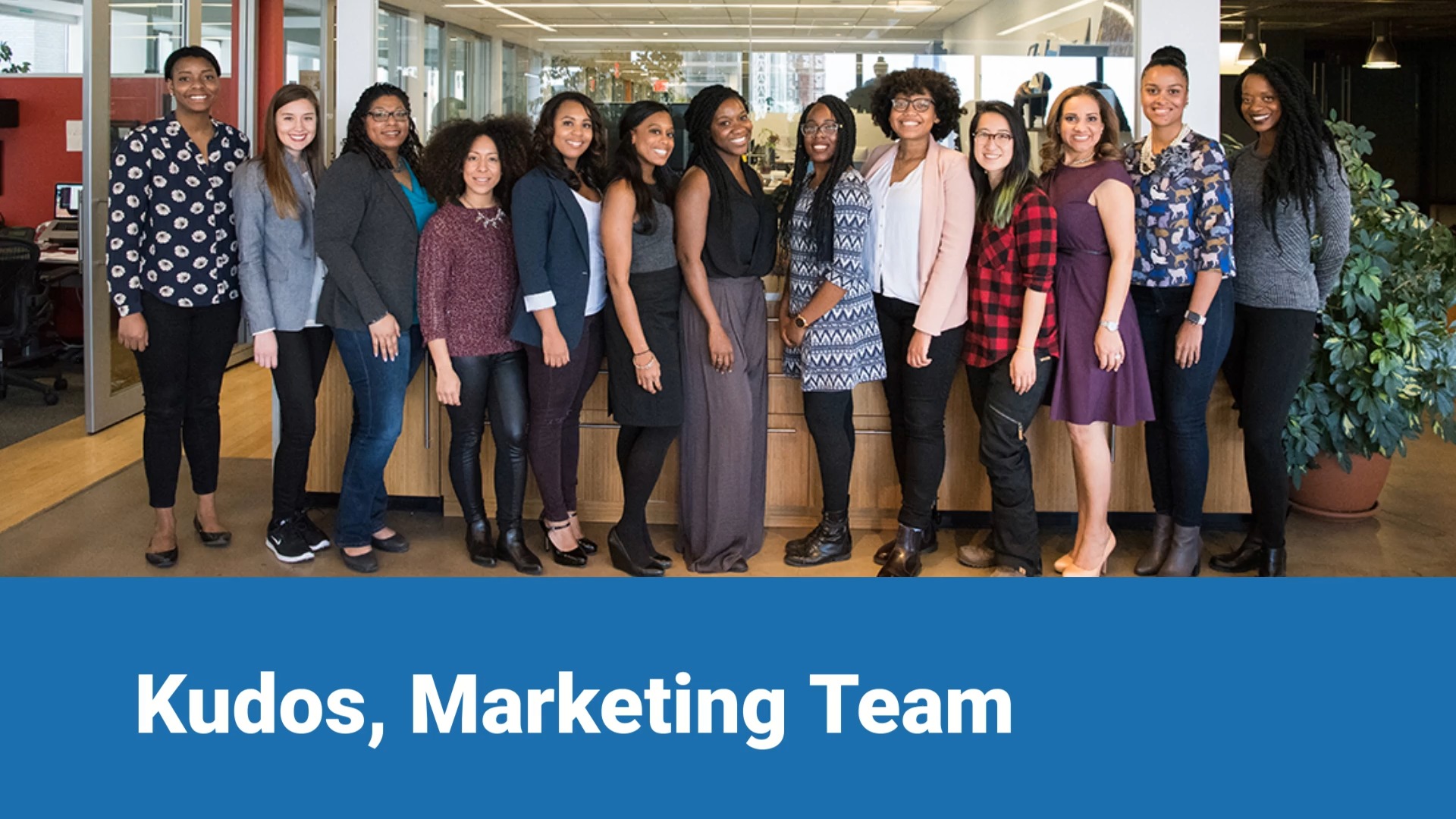 Group of diverse women smiling in an office environment with text "Kudos, Marketing Team" at the bottom.