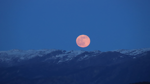 A Full Moon rises over snowy mountains.