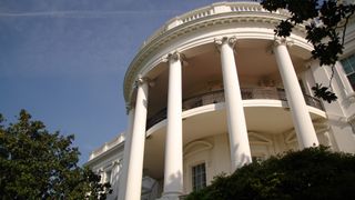 White House South Portico pictured from below with blue sky and trees in foreground