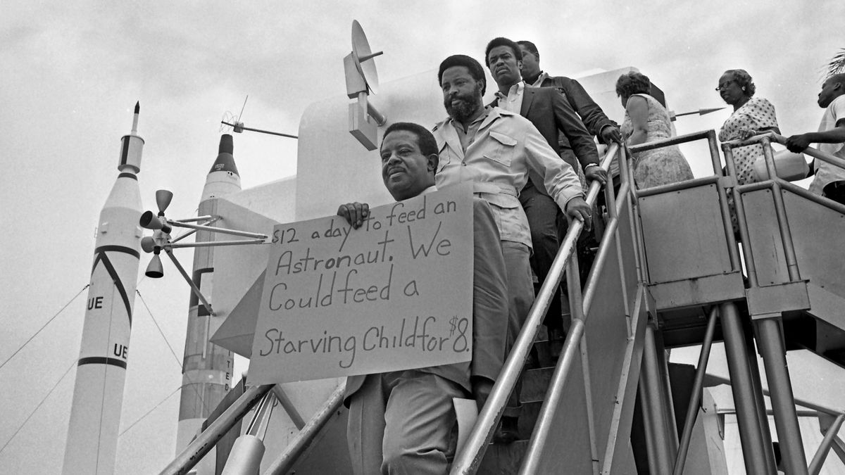 Reverend Ralph Abernathy holds a sign protesting poverty in the U.S. at the Apollo 11 launch.