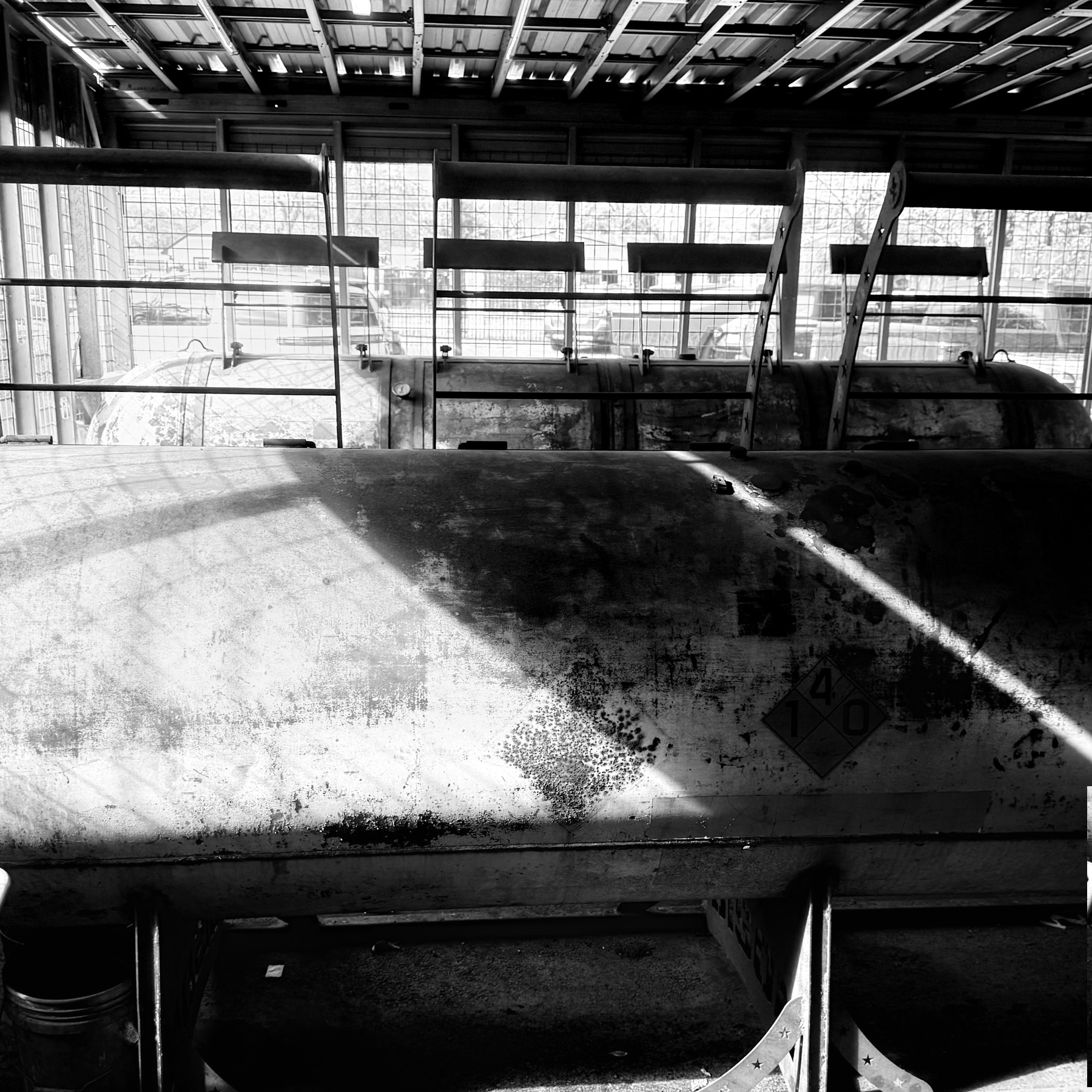 A black and white photograph features an industrial setting with large metal smokers inside a structure with a grid-like ceiling.