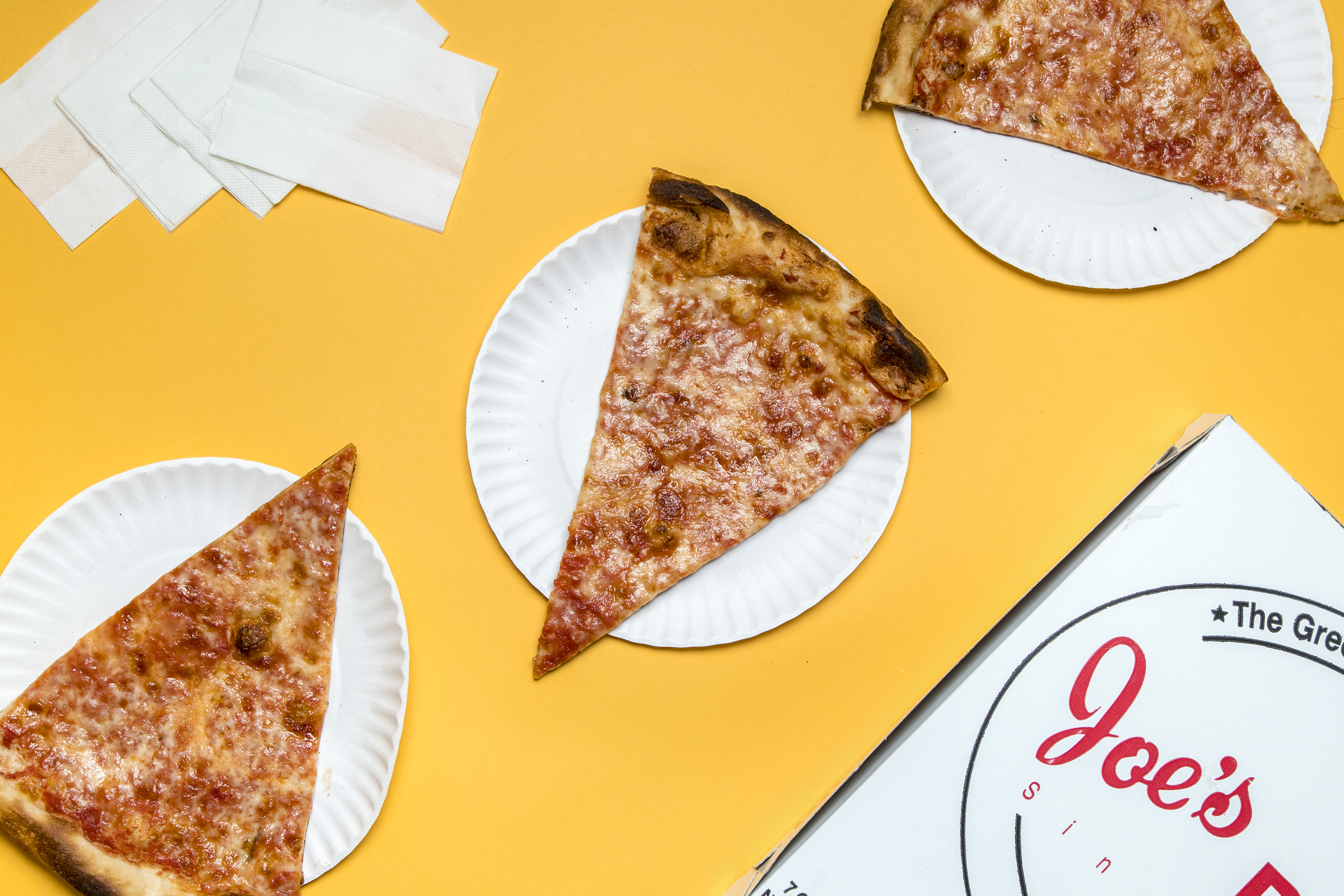 An overhead photograph of a yellow table with a greasy slice of pizza from Joe’s.