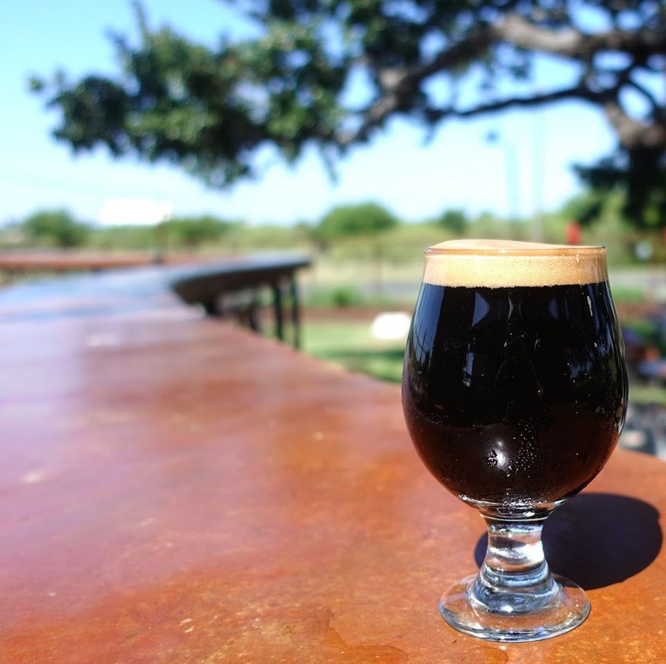 A dark beer sitting outside on a long table with a tree in the background