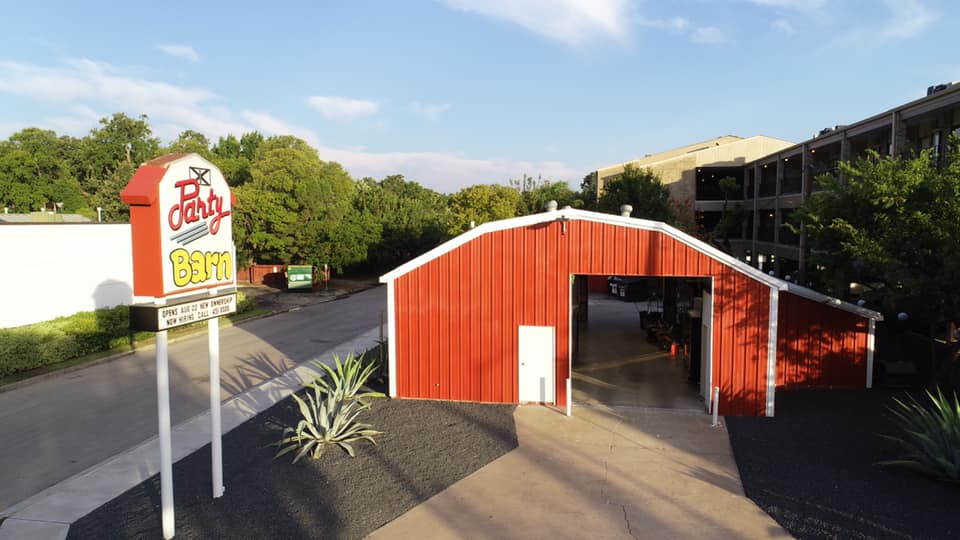 The drive-thru at a red barn like building with a sign to the left and condos in the background on a day with clear blue skies