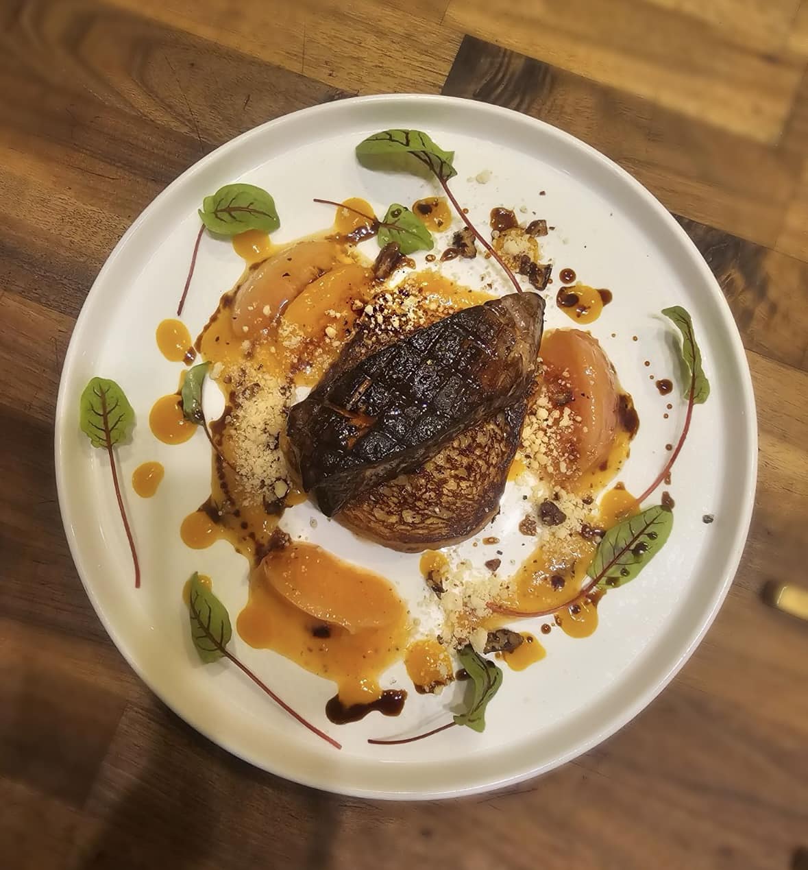 A piece of foie with fruit, leaves, and nuts surrounding it.