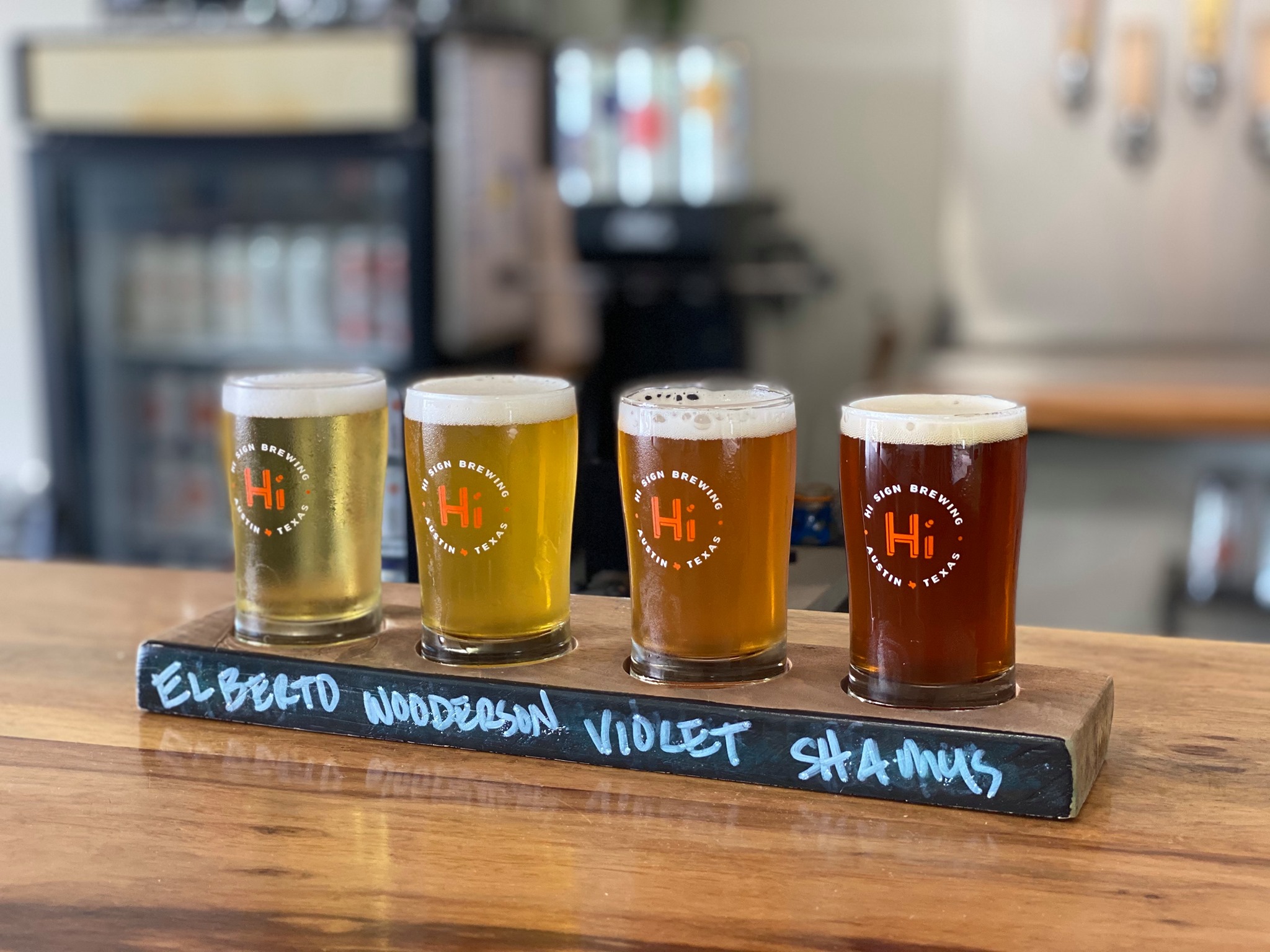 Four beers in pint glasses on a board with the names written in chalk