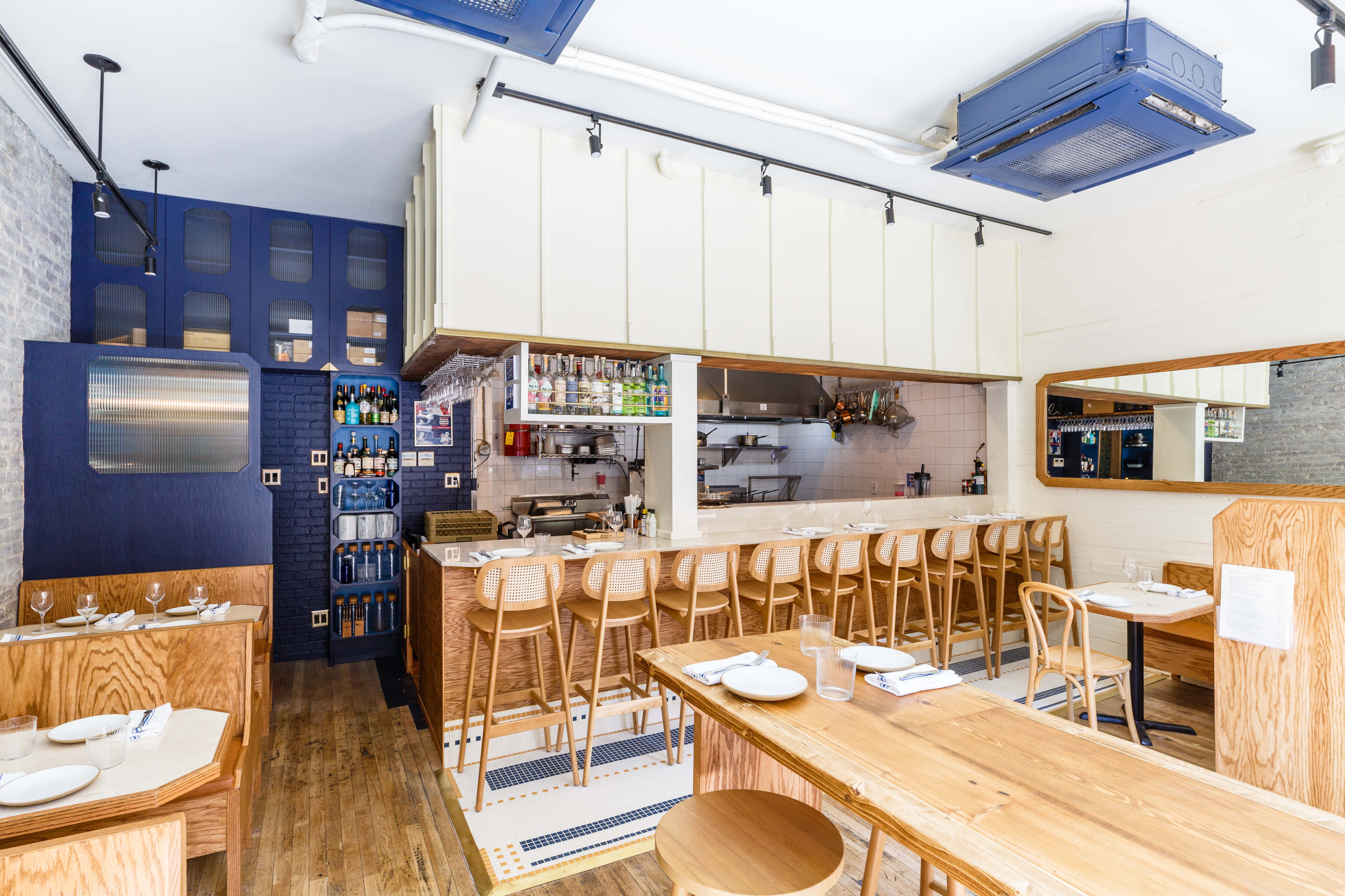 An interior of a restaurant with a bar overlooking an open kitchen and wooden booths around the perimeter