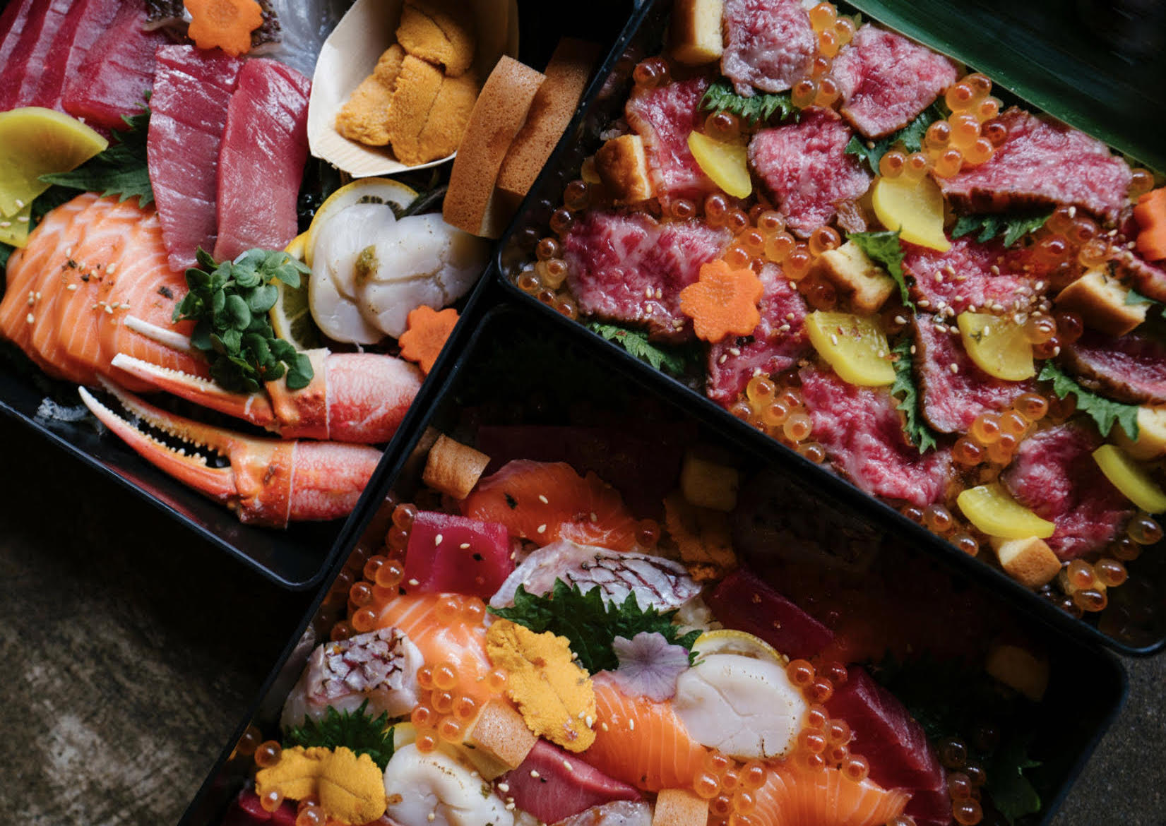 An overhead triptych of bento/chirashi boxes in dim lighting.