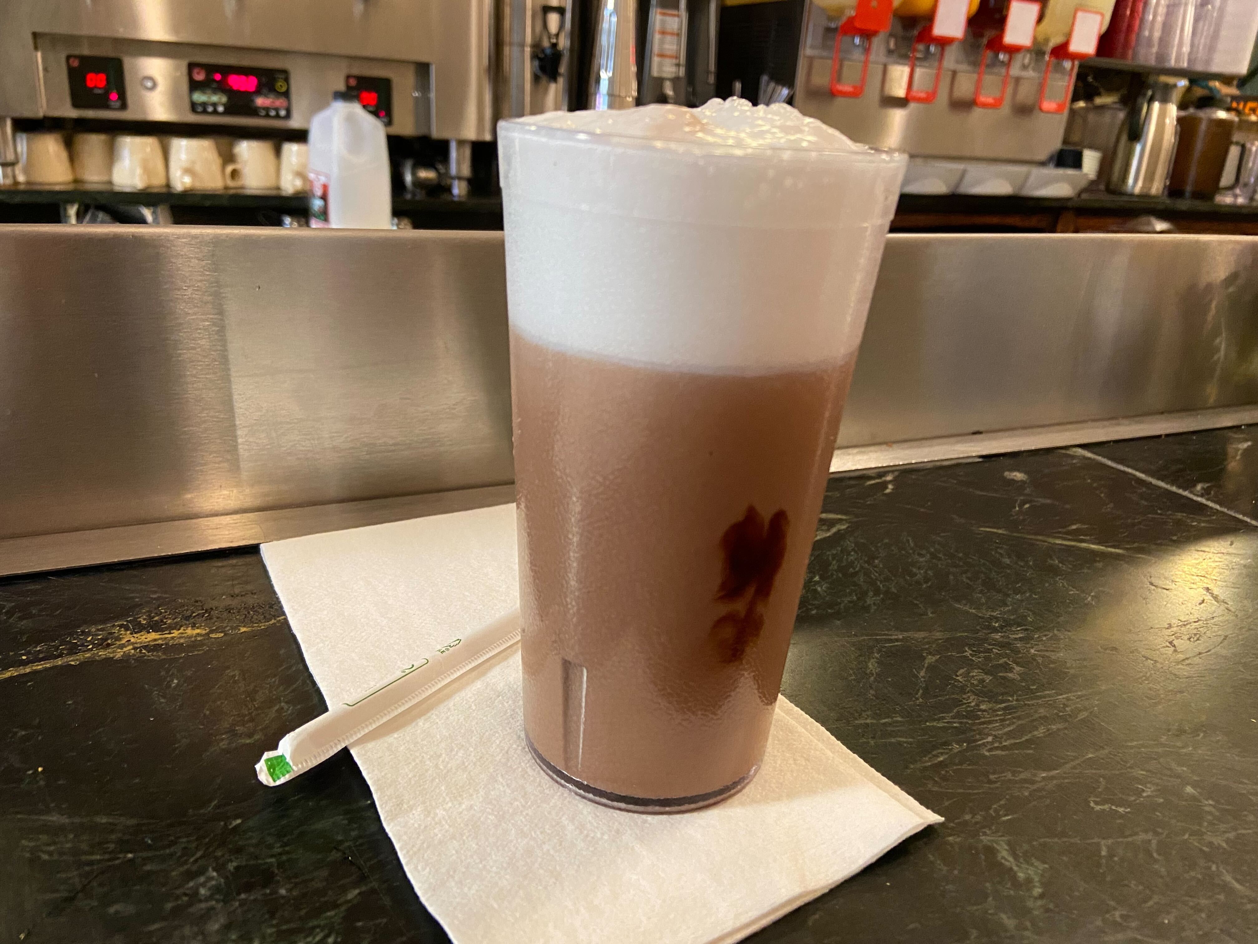 A chocolate egg cream sits on a counter with a plastic straw and white napkin.